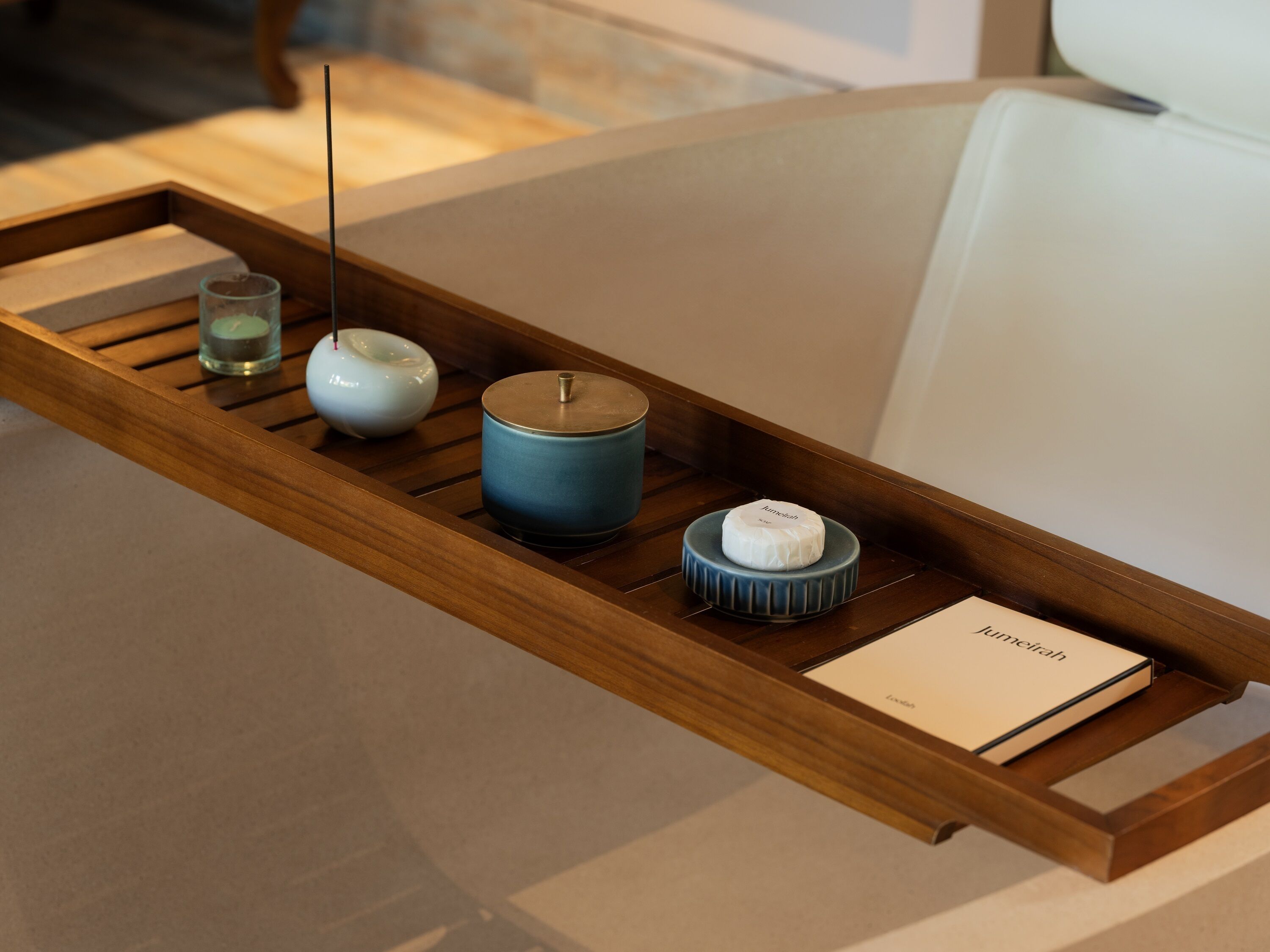 A wooden tray with a candle, a blue container, and a small white object on a table.