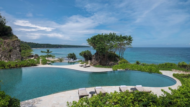 A pool with a curved edge, surrounded by greenery and a view of the sea. - Jumeirah Bali (Pecatu)