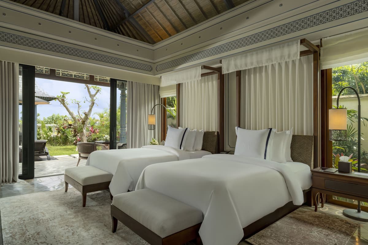A hotel room with two beds, a sitting area, and a view of the outdoors.