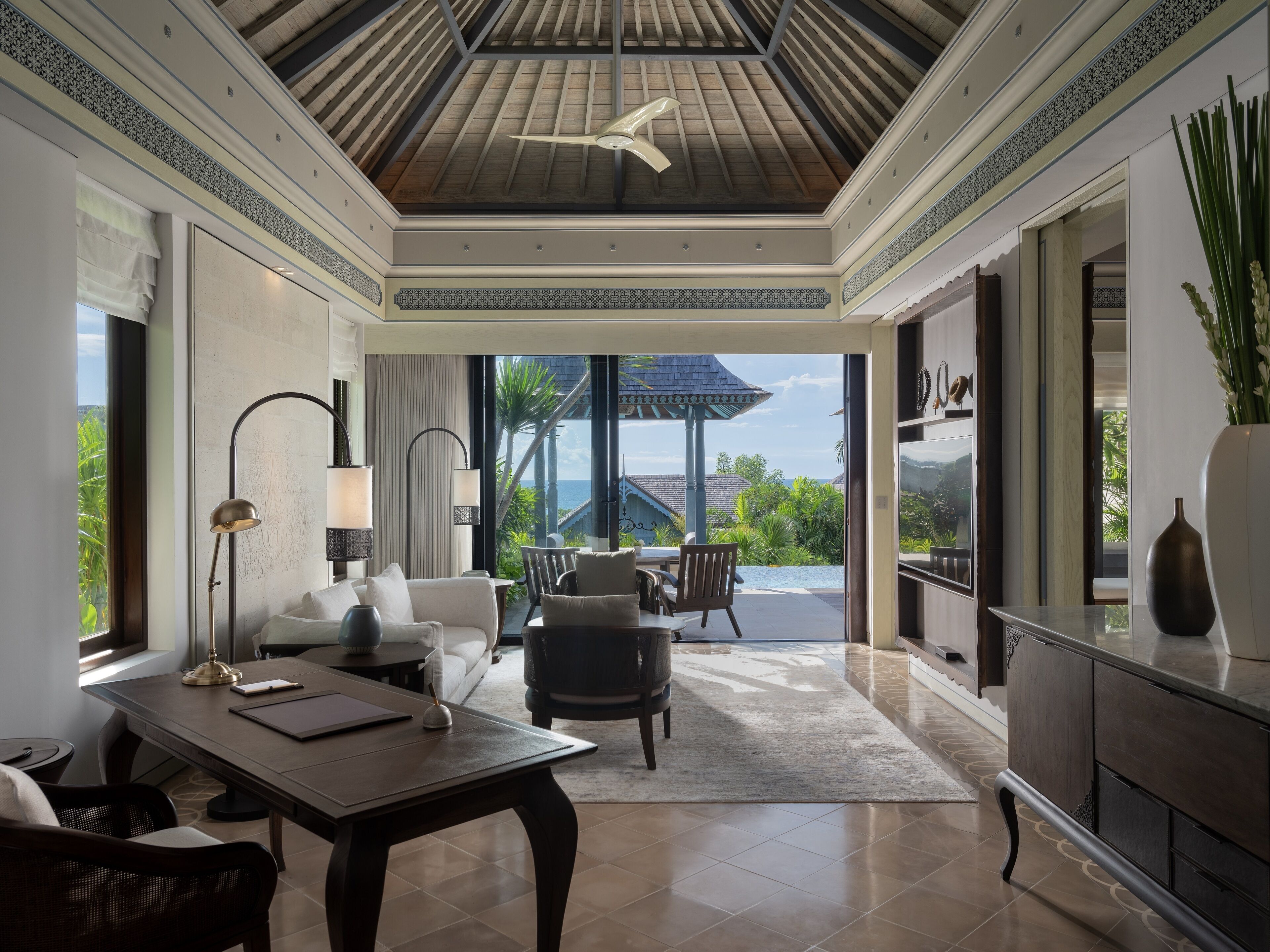 A spacious room with a large dining table, comfortable seating, a ceiling fan, and a view of the ocean.