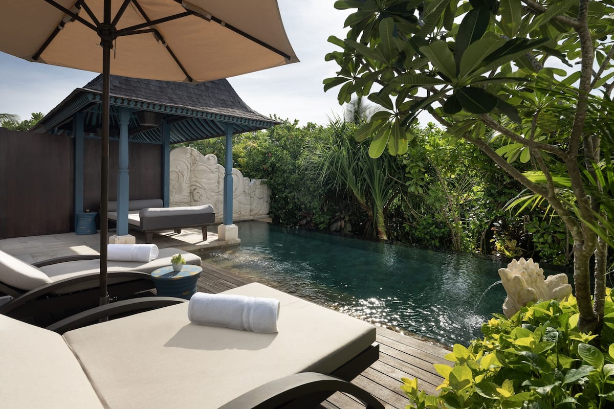 A poolside area with lounge chairs, a pergola, and a stone wall.