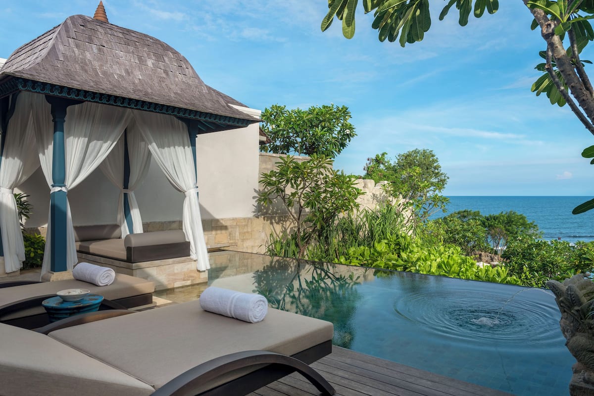 A serene poolside area with a lounge chair, a small gazebo, and a view of the ocean.