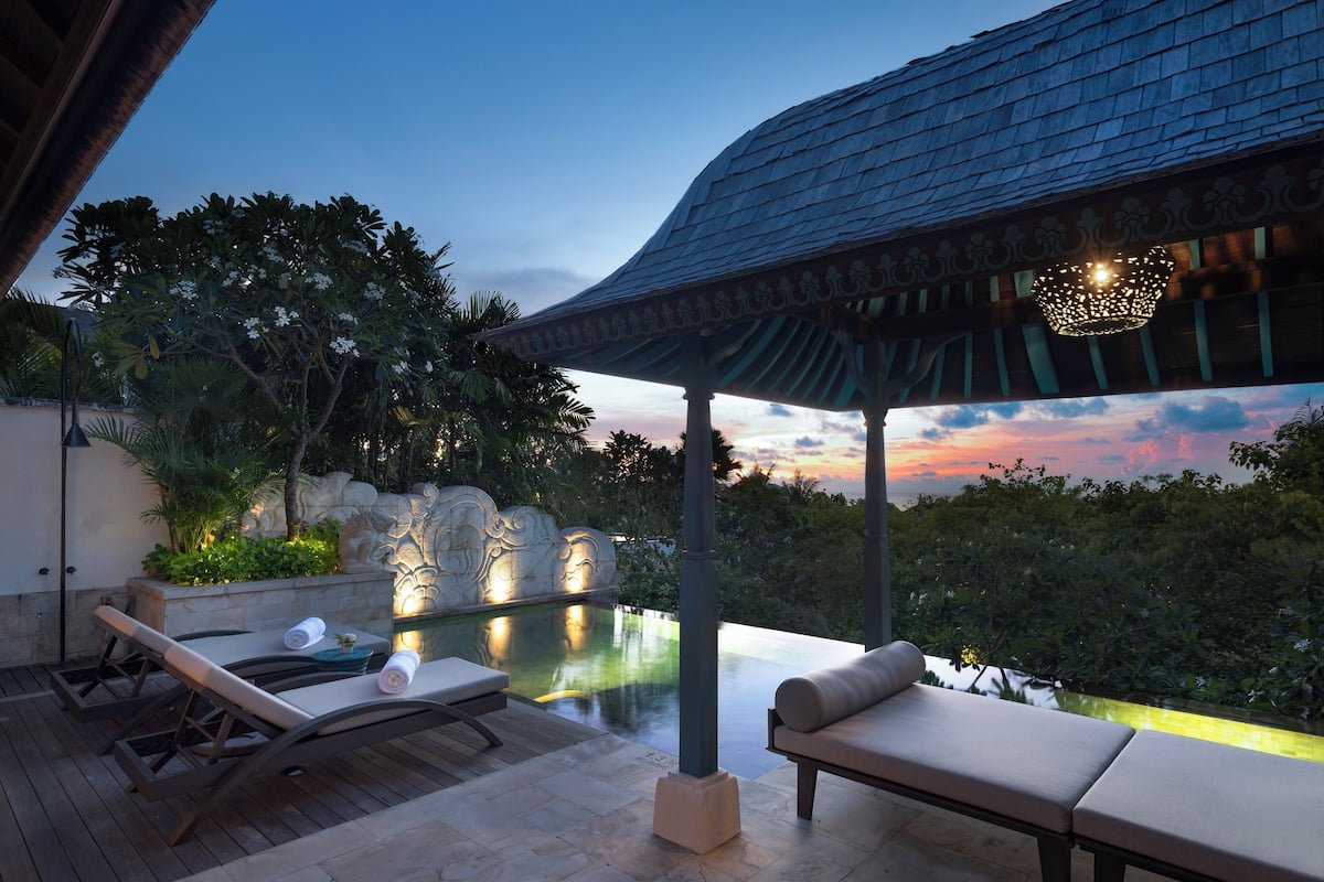 A serene outdoor lounge area with a pool, lounge chairs, and a decorative ceiling.
