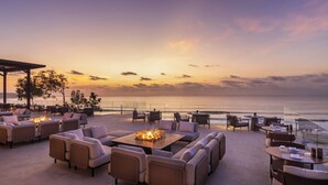 A beachside patio with outdoor seating, a fire pit, and a view of the ocean at sunset. - Jumeirah Bali (Pecatu)