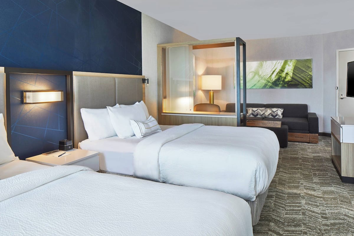 Une chambre d’hôtel avec deux lits, un bureau, une chaise, un canapé et un grand miroir.