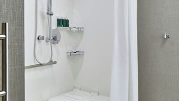 Área de chuveiro moderna com divisória de vidro, chuveiro manual e toalheiro branco.