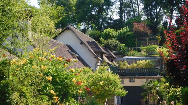 A residential area with a house featuring a sloped roof and a small garden with various plants and flowers. - "from one Eure to another" A charming house in a garden (SAINTE GEMME MORONVAL)