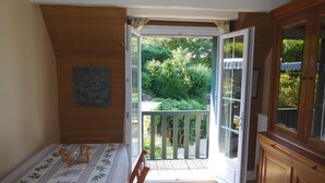 A room with a dining table set for two, a wooden cabinet, and a sliding glass door leading to a balcony with a view of greenery. - "from one Eure to another" A charming house in a garden (SAINTE GEMME MORONVAL)