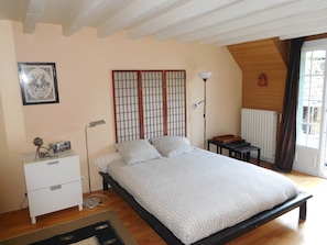 A bedroom with a bed, bedside table, lamp, radiator, and a window with curtains.