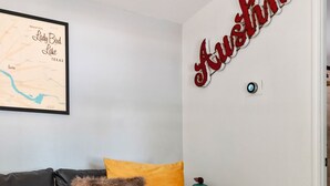 A living room with a black sofa, a wooden coffee table, a yellow pillow, a map on the wall, and a sign that reads "Austin". - Lady Bird House ATX walk to Rainey, Cesar Chavez and 6 street (Austin)