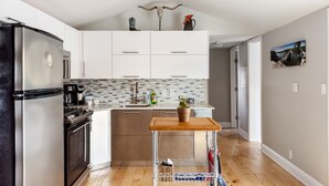 A modern kitchen with white cabinets, a stainless steel refrigerator, and a wooden table. - Lady Bird House ATX walk to Rainey, Cesar Chavez and 6 street (Austin)