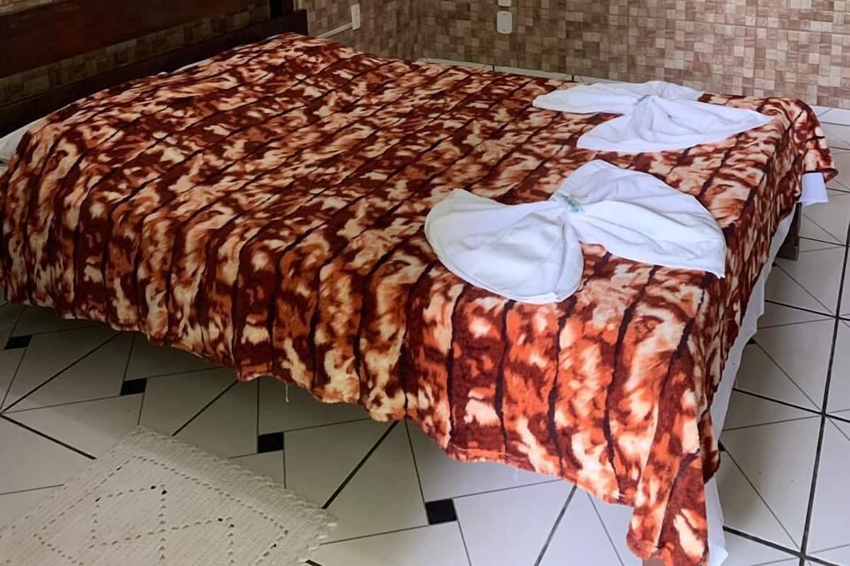 Habitación de hotel con cama, cabecera de madera, suelo de baldosas y papel tapiz estampado.