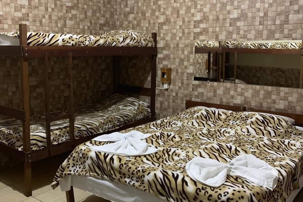 Una habitación con tres literas, cada una con un edredón estampado con diseño de cebra. Hay un espejo pequeño sobre la litera más a la derecha y un felpudo blanco en el suelo.
