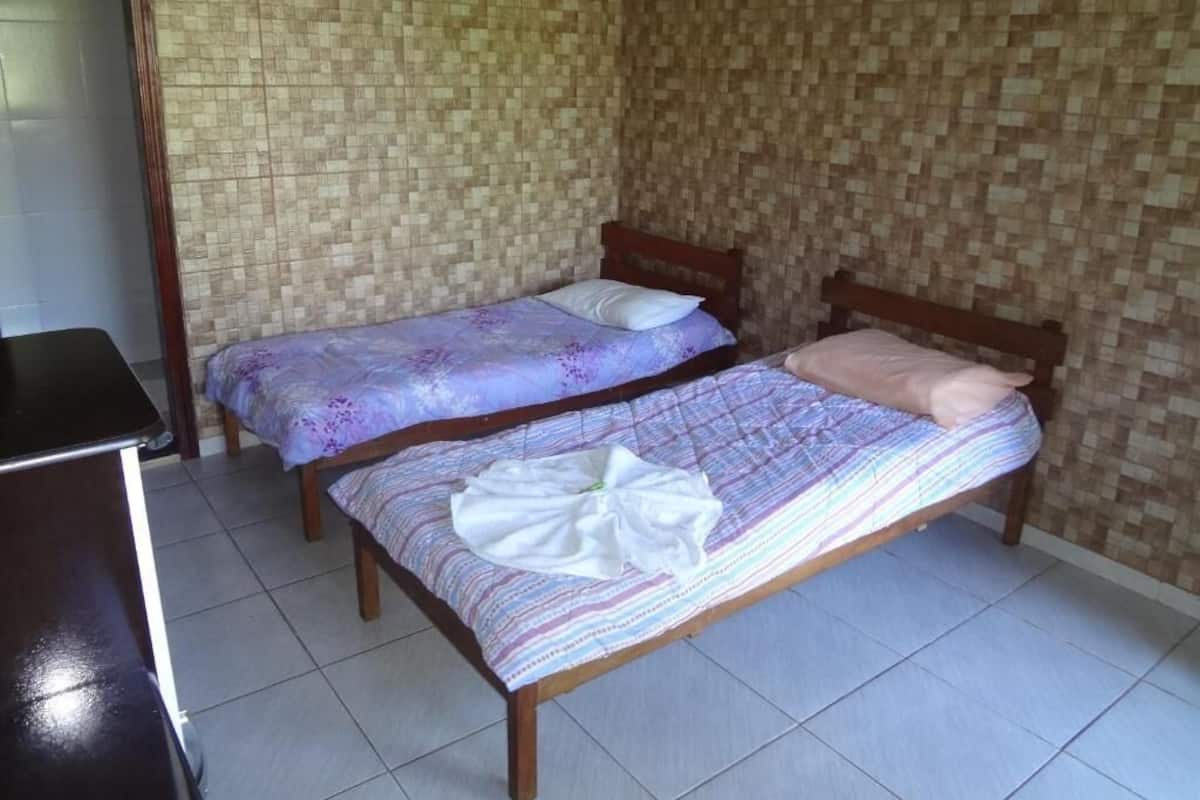 Una habitación pequeña con dos camas de madera, piso de baldosas y un papel tapiz estampado.