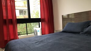 A bedroom with a bed, red curtains, and a window with a view of buildings and trees. - Apartamentos Charcas (Buenos Aires)