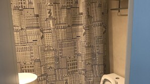 A bathroom with a toilet, sink, and shower curtain with a cityscape design. - Apartamentos Charcas (Buenos Aires)
