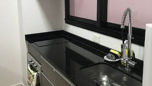 A compact kitchen with a black countertop, a stainless steel sink, a faucet, a microwave, and a window above the sink. - Apartamentos Charcas (Buenos Aires)
