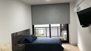 A modern bedroom with a bed, a nightstand, a TV mounted on the wall, and a window with a view of the outside. - Apartamentos Charcas (Buenos Aires)