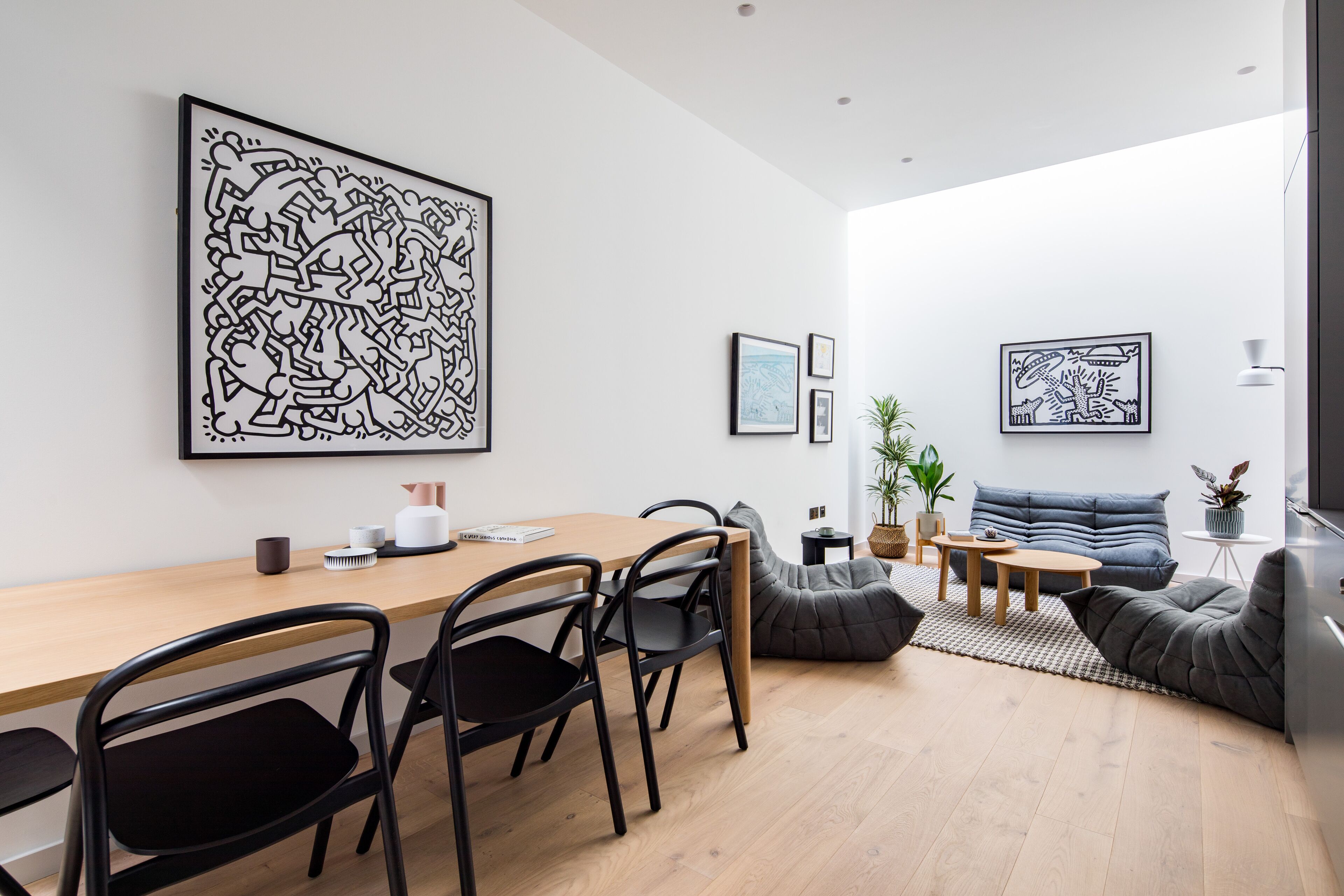 A modern living room with a wooden dining table, black chairs, a grey sofa, and a large abstract artwork on the wall.