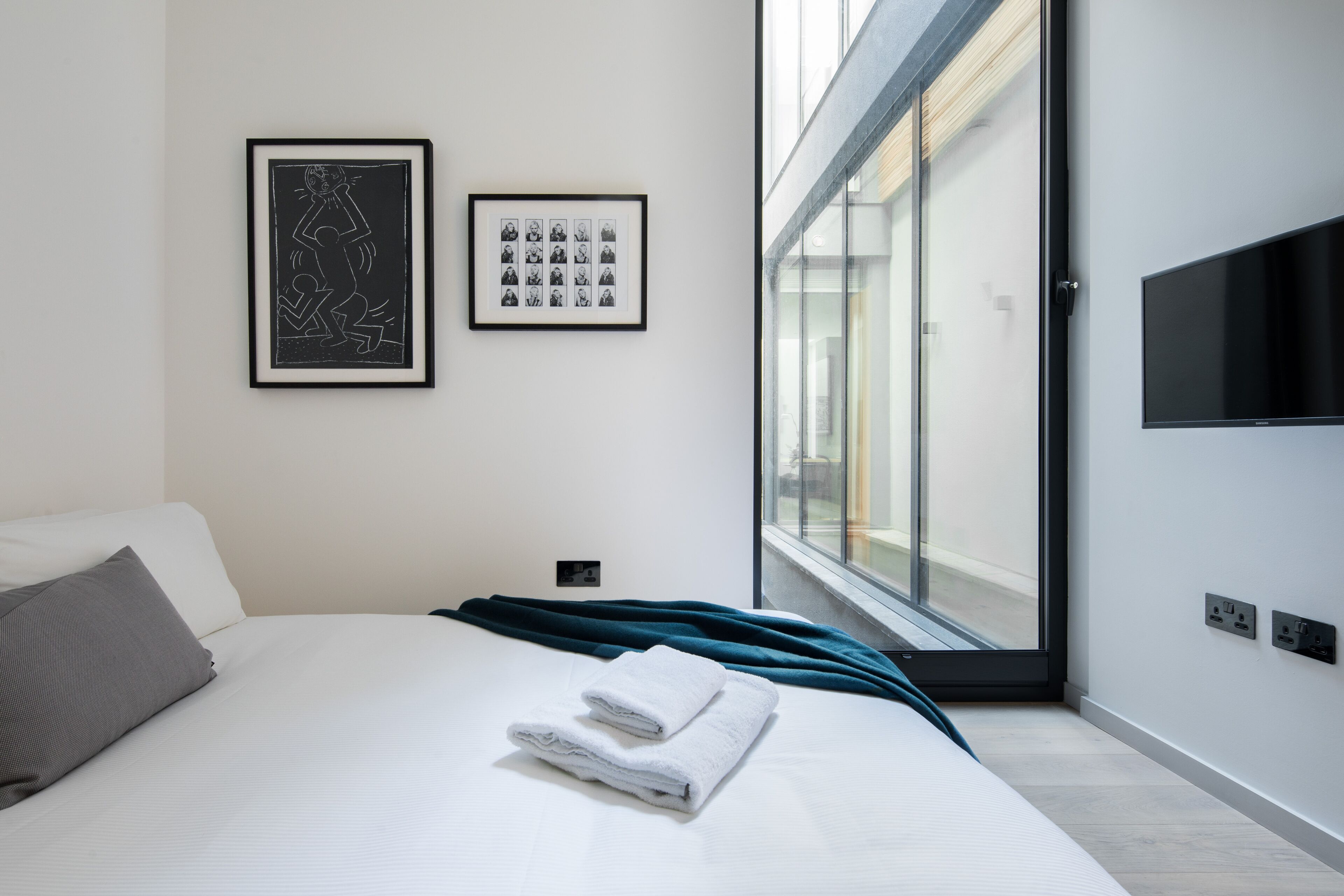 A modern hotel room with a large bed, a flat-screen TV mounted on the wall, and a window providing a view of the outside.