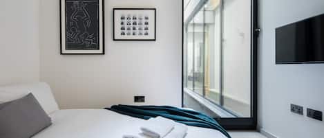 A modern hotel room with a large bed, a flat-screen TV mounted on the wall, and a window providing a view of the outside.