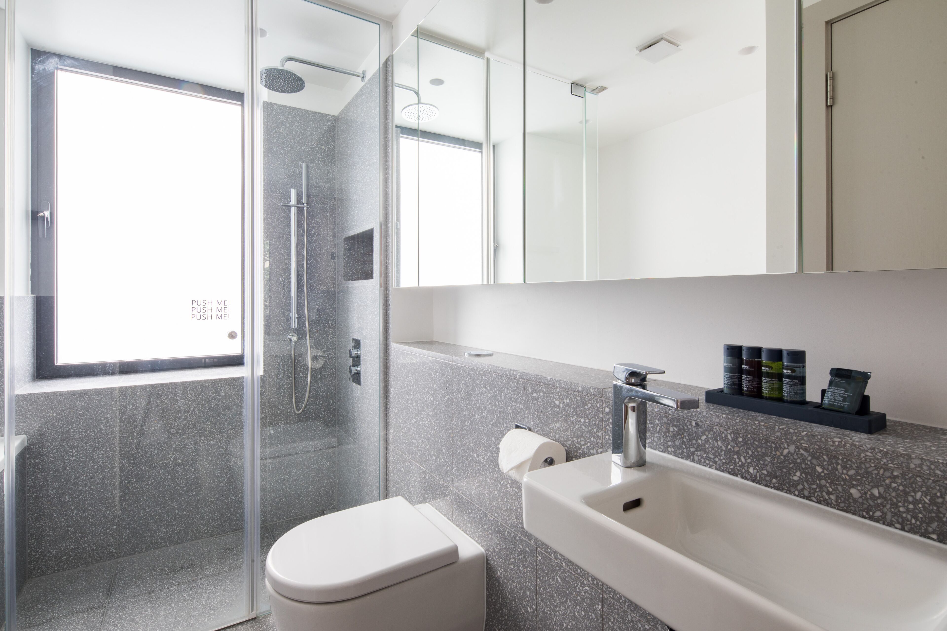 A modern bathroom with a glass-enclosed shower, a white toilet, and a sink with a mirror above.