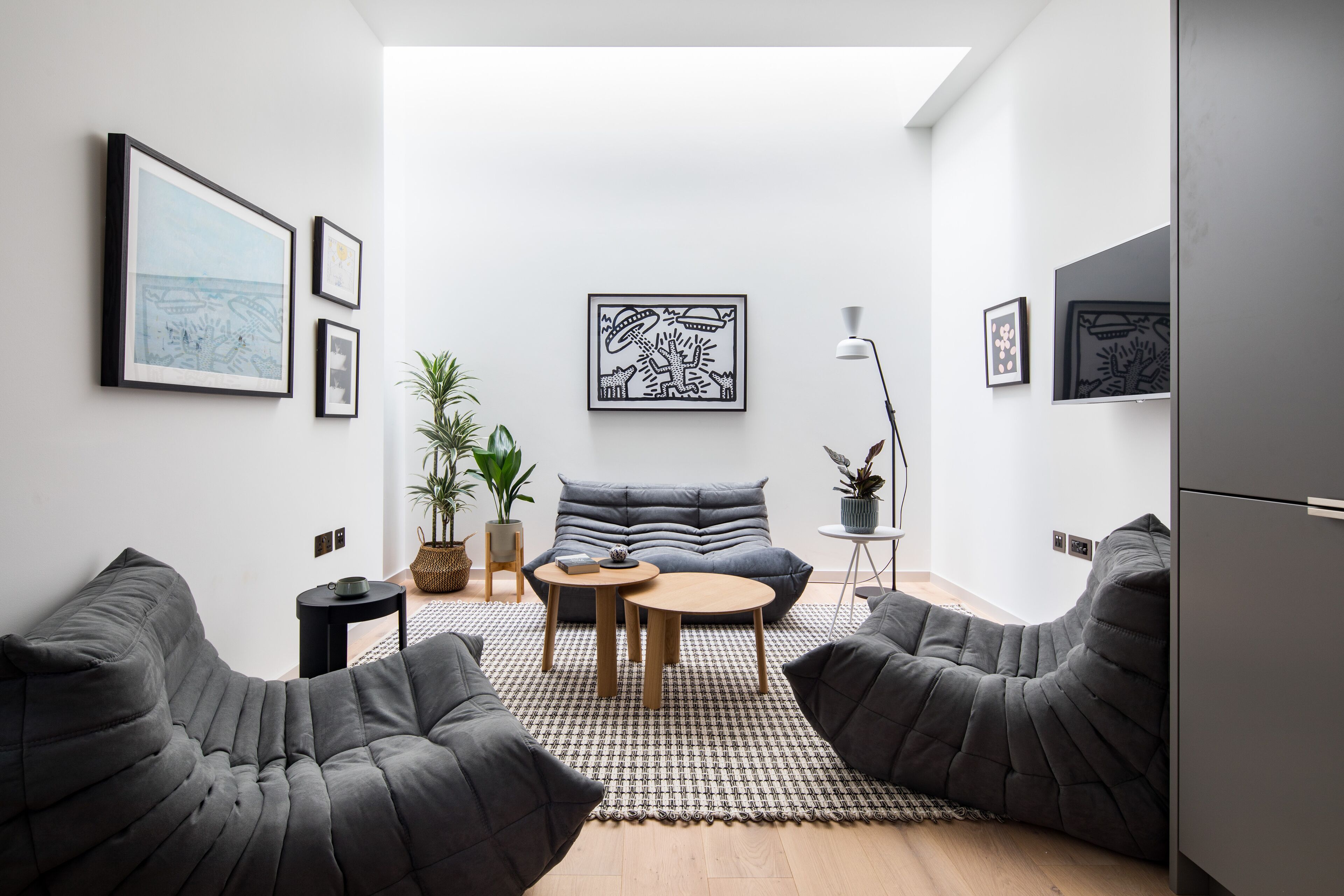 A modern living room with a sofa, two armchairs, a coffee table, and a floor lamp. There are framed artworks on the walls and a potted plant on the floor.