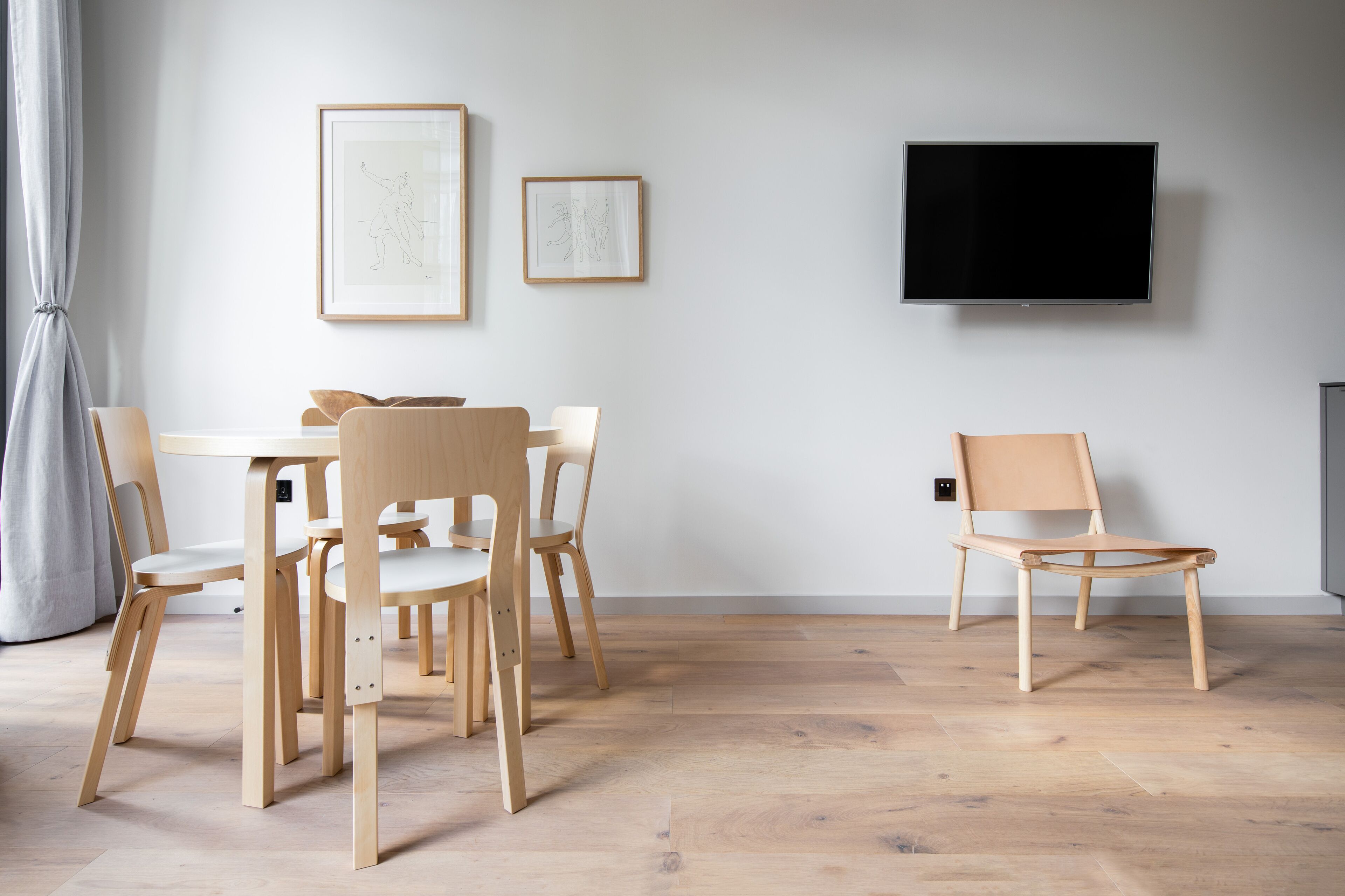 Ein modernes Wohnzimmer mit Esstisch, Stühlen, einem Flachbildfernseher und gerahmten Kunstwerken an der Wand.