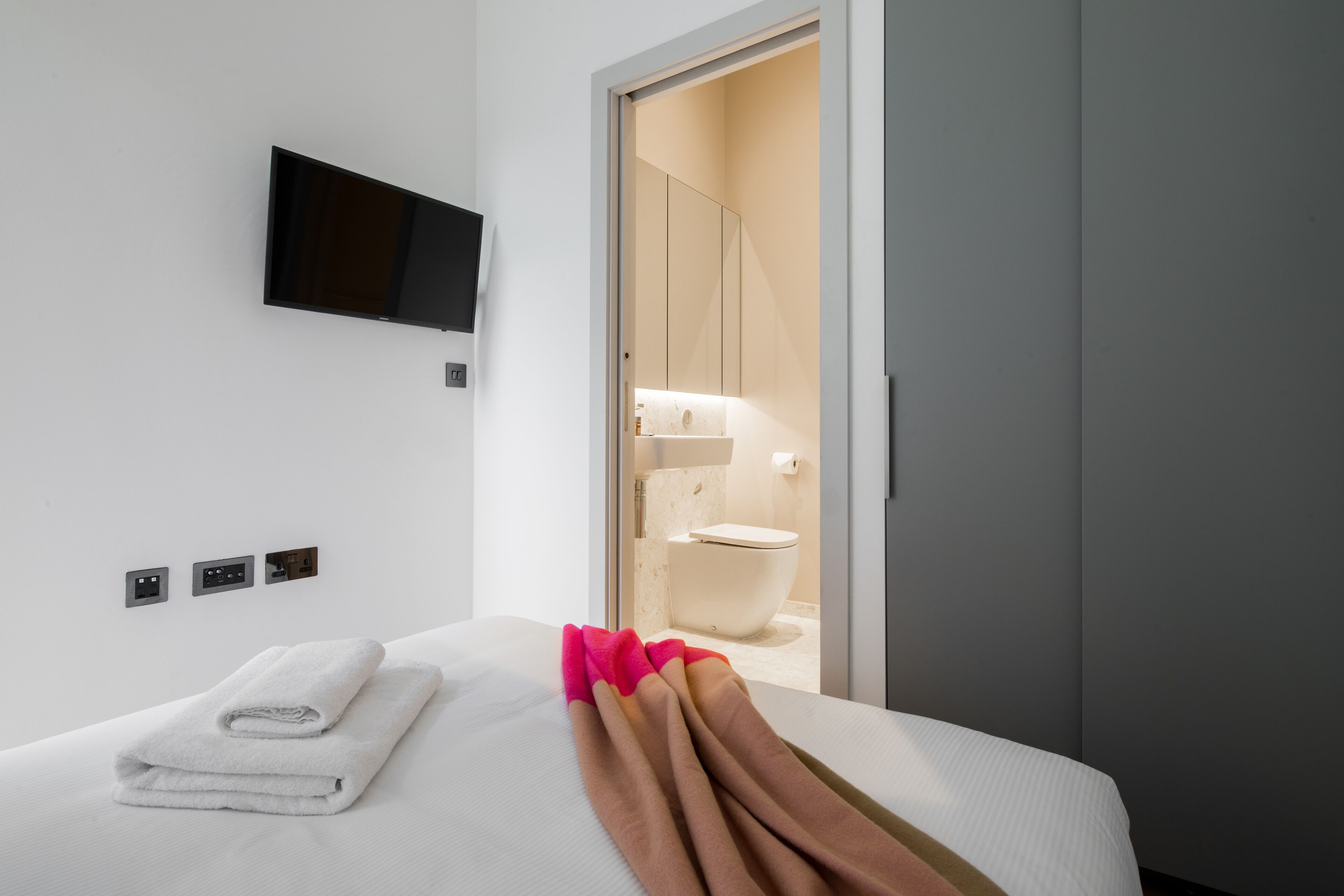 Une chambre d’hôtel avec un lit, un téléviseur à écran plat fixé au mur et une salle de bain visible à travers une porte ouverte.