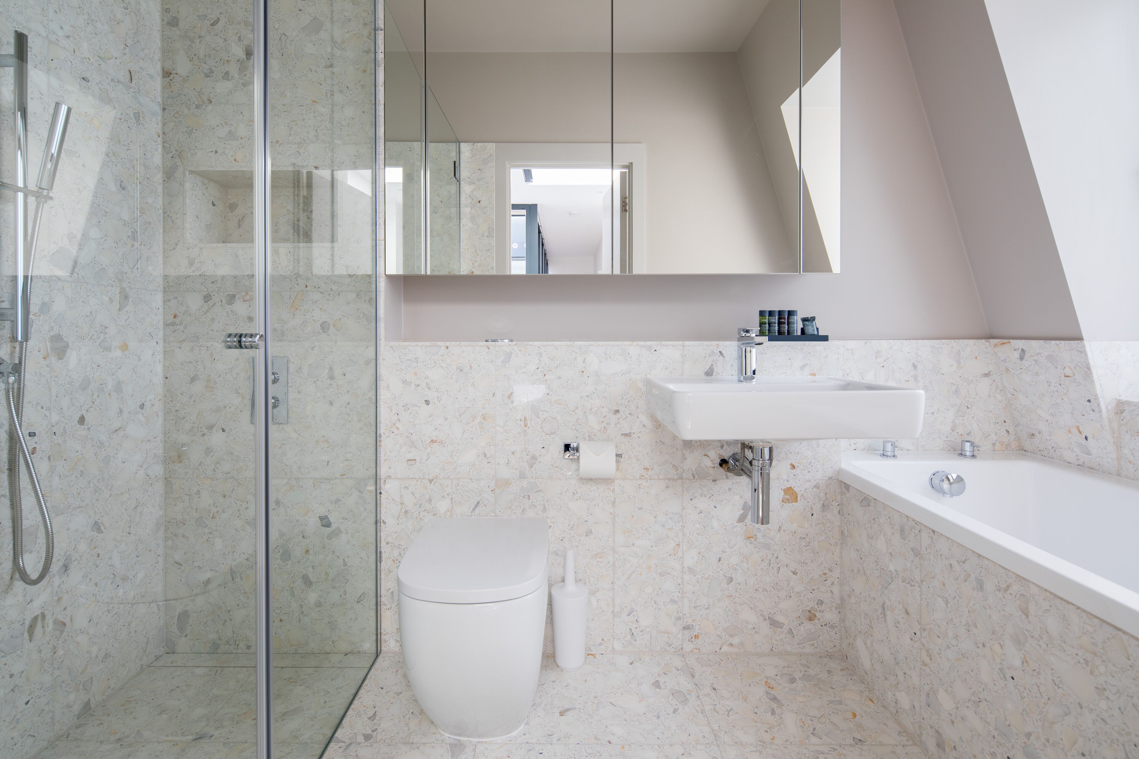 A modern bathroom with a glass-enclosed shower, a white toilet, and a sink with a mirror above.