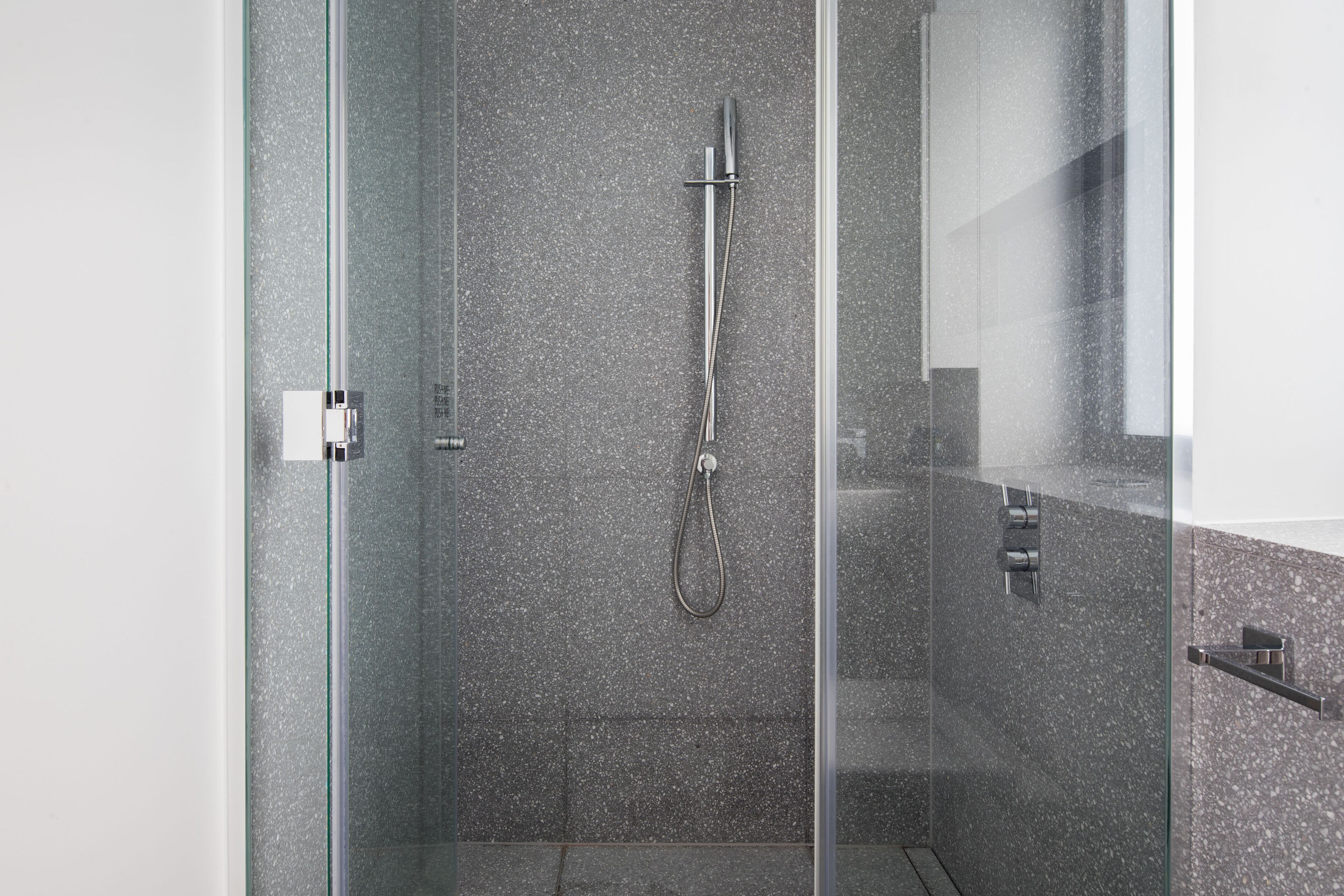 A modern shower with a glass door, a handheld showerhead, and a wall-mounted control panel.