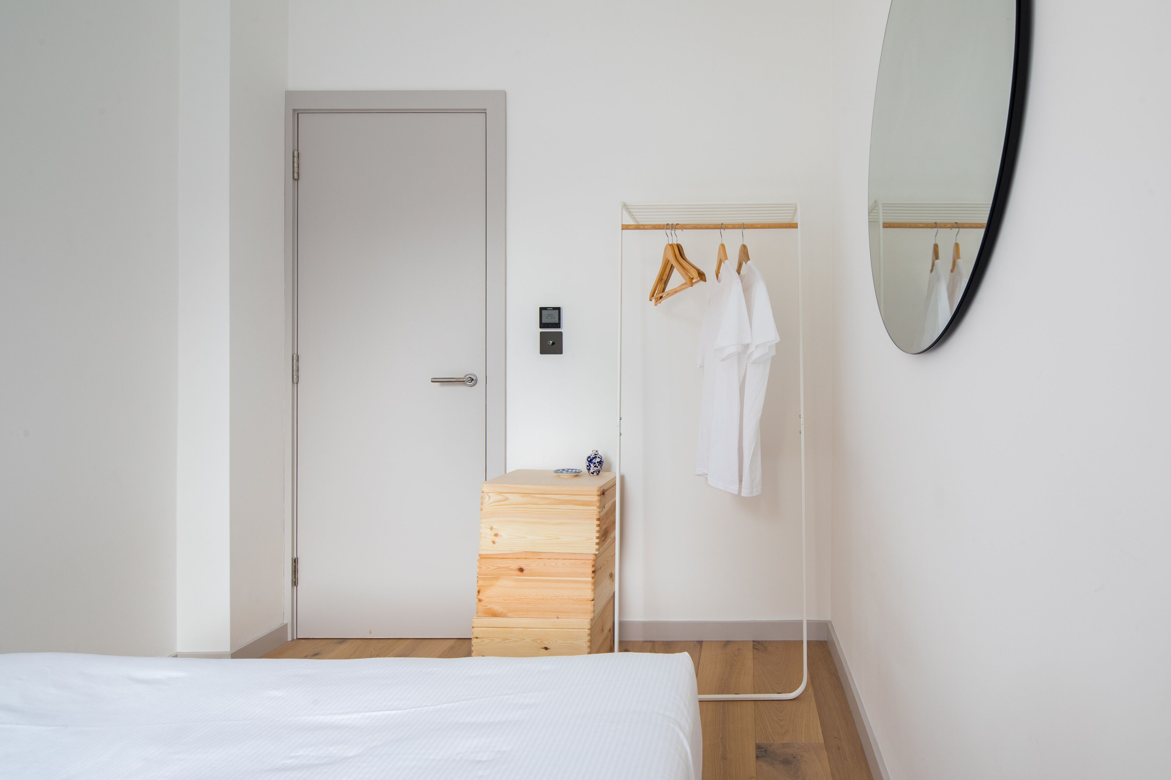 Une chambre à coucher avec un lit, une commode en bois, une armoire remplie de vêtements, une porte et un miroir accroché au mur.