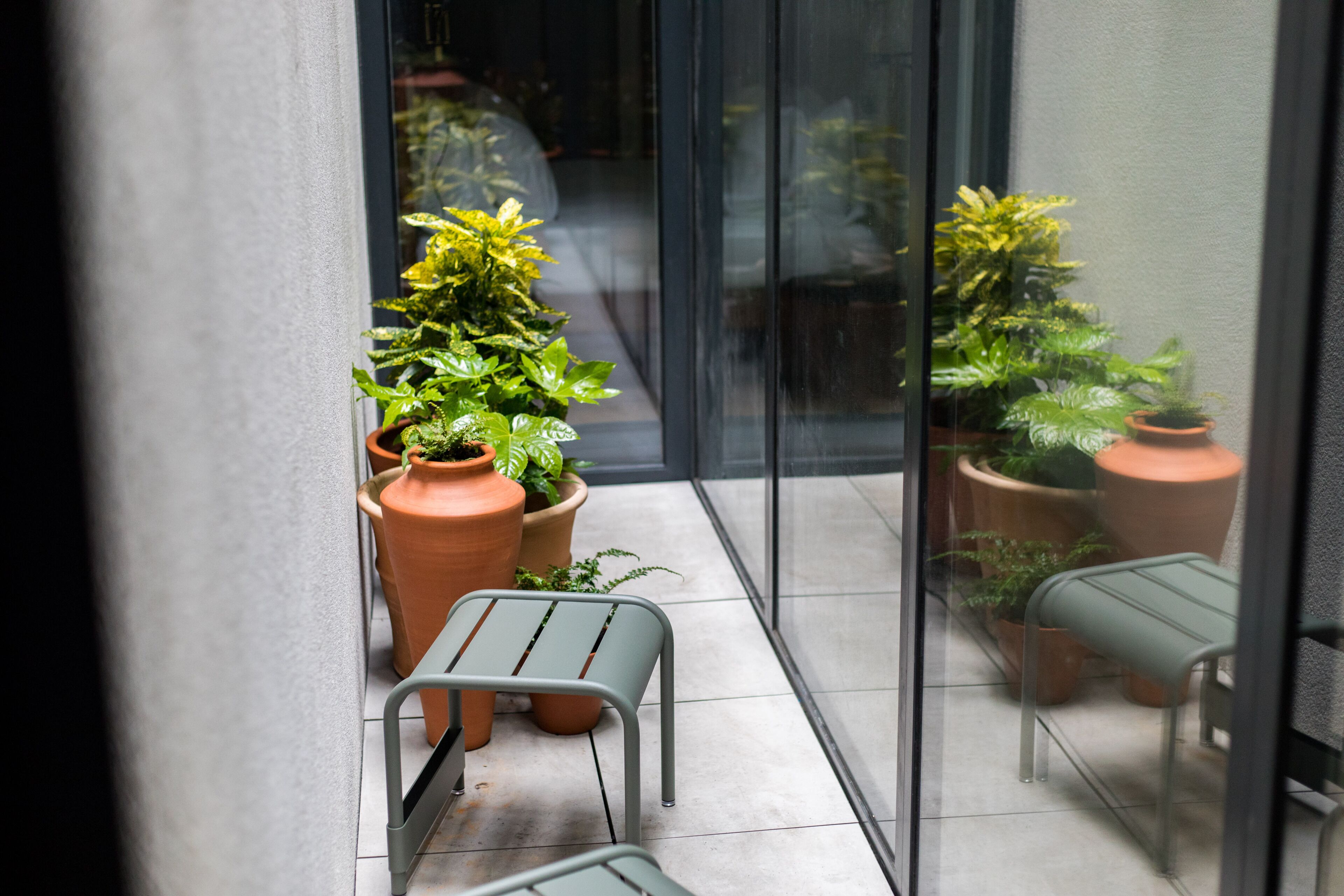 A small, enclosed balcony with terracotta planters and metal chairs.