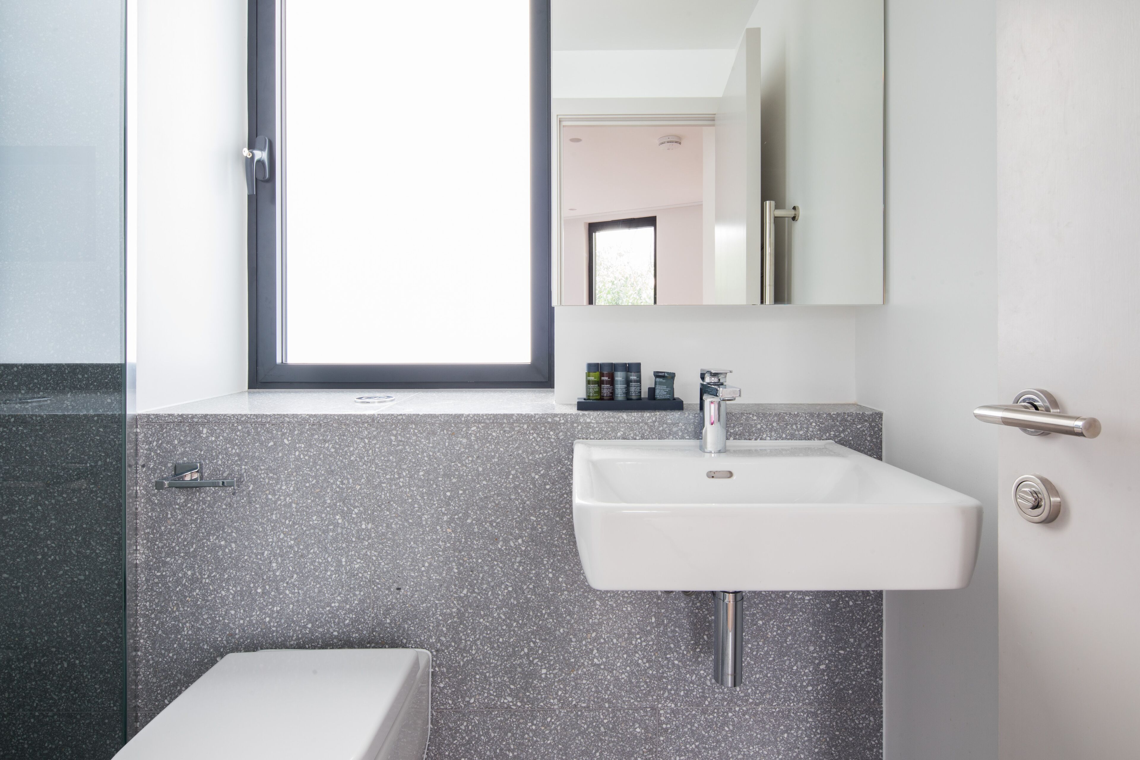 A modern bathroom with a white sink, a mirror, and a window.
