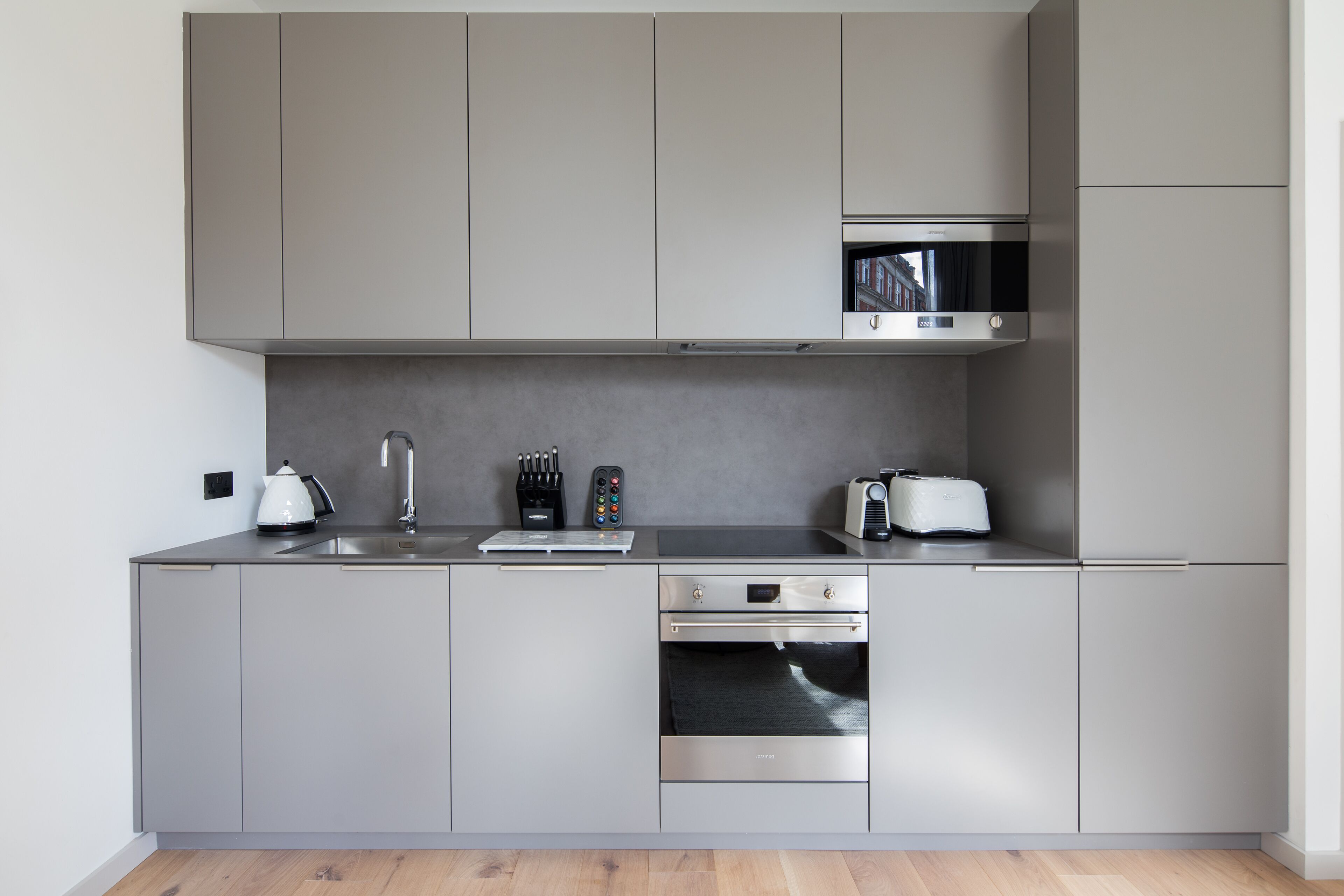 A modern kitchen with grey cabinets, a stainless steel oven, a microwave, and a toaster.
