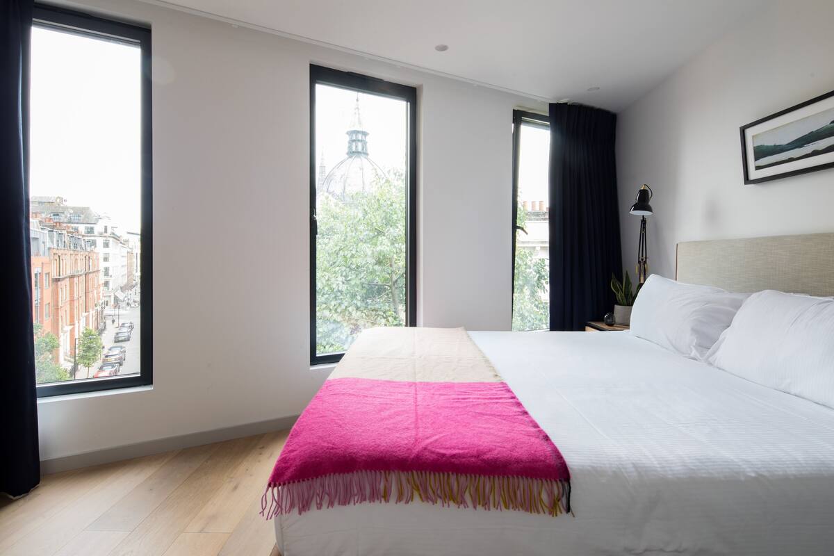 A hotel room with a large bed, a view of the city through large windows, and a cityscape visible through the windows.