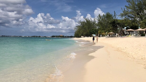 A beach with clear turquoise water, a sandy shore, and a row of beachside huts with umbrellas. - Relax at Coconut Bay! (West Bay)
