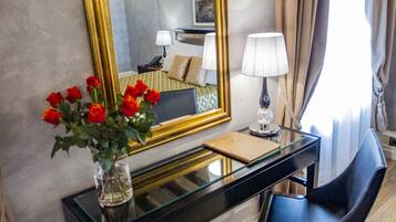 Une chambre d’hôtel avec un grand miroir, un bureau agrémenté d’un vase de roses rouges, une chaise et un lit avec une literie à motifs.