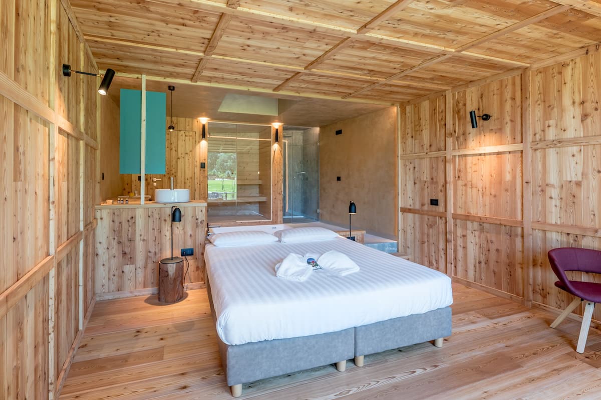 A wooden cabin-style bedroom with a bed, bedside tables, and a mirror.