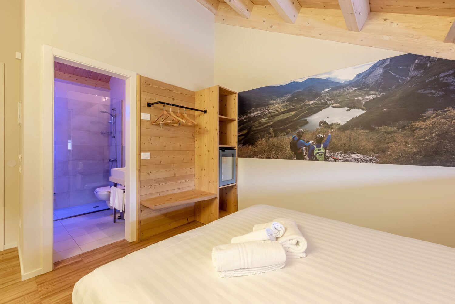 Ein Schlafzimmer mit Bett, Holzschrank, Dusche und großem Wandbild mit einer Berglandschaft.