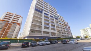 Un edificio residencial de varios pisos, con balcones y un estacionamiento al frente.
