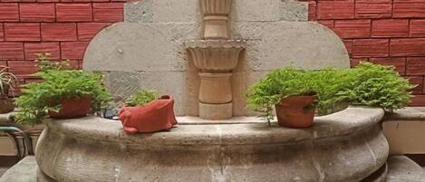 A stone fountain with a central column and two potted plants on either side.