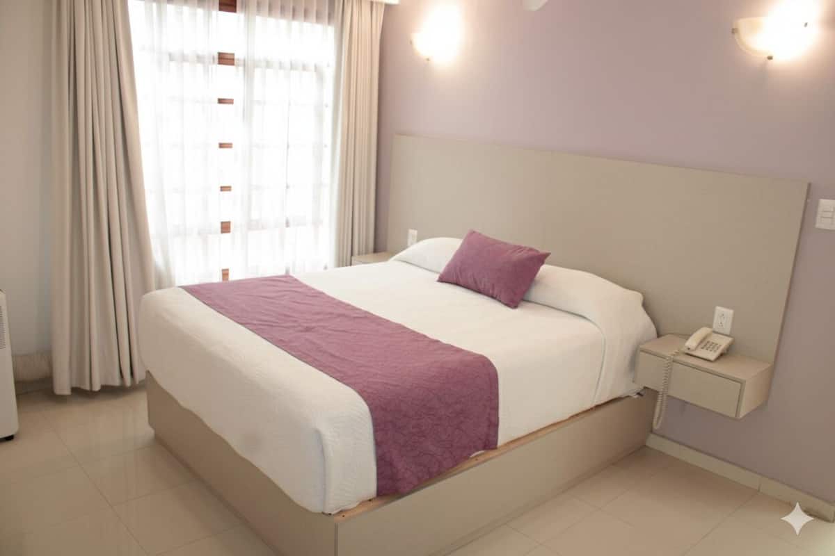 A hotel room with a bed, a nightstand, a telephone, and a window with curtains.