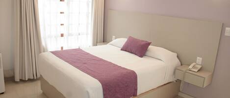 A hotel room with a bed, a nightstand, a telephone, and a window with curtains.
