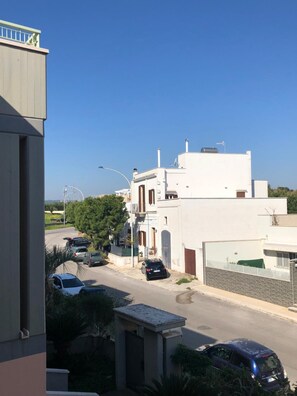Una calle residencial con edificios blancos, coches aparcados y un cielo azul despejado.