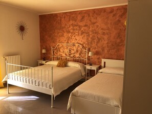 Habitación de hotel con dos camas, un radiador, un adorno de sol colgado en la pared y dos mesitas de noche con lámparas.