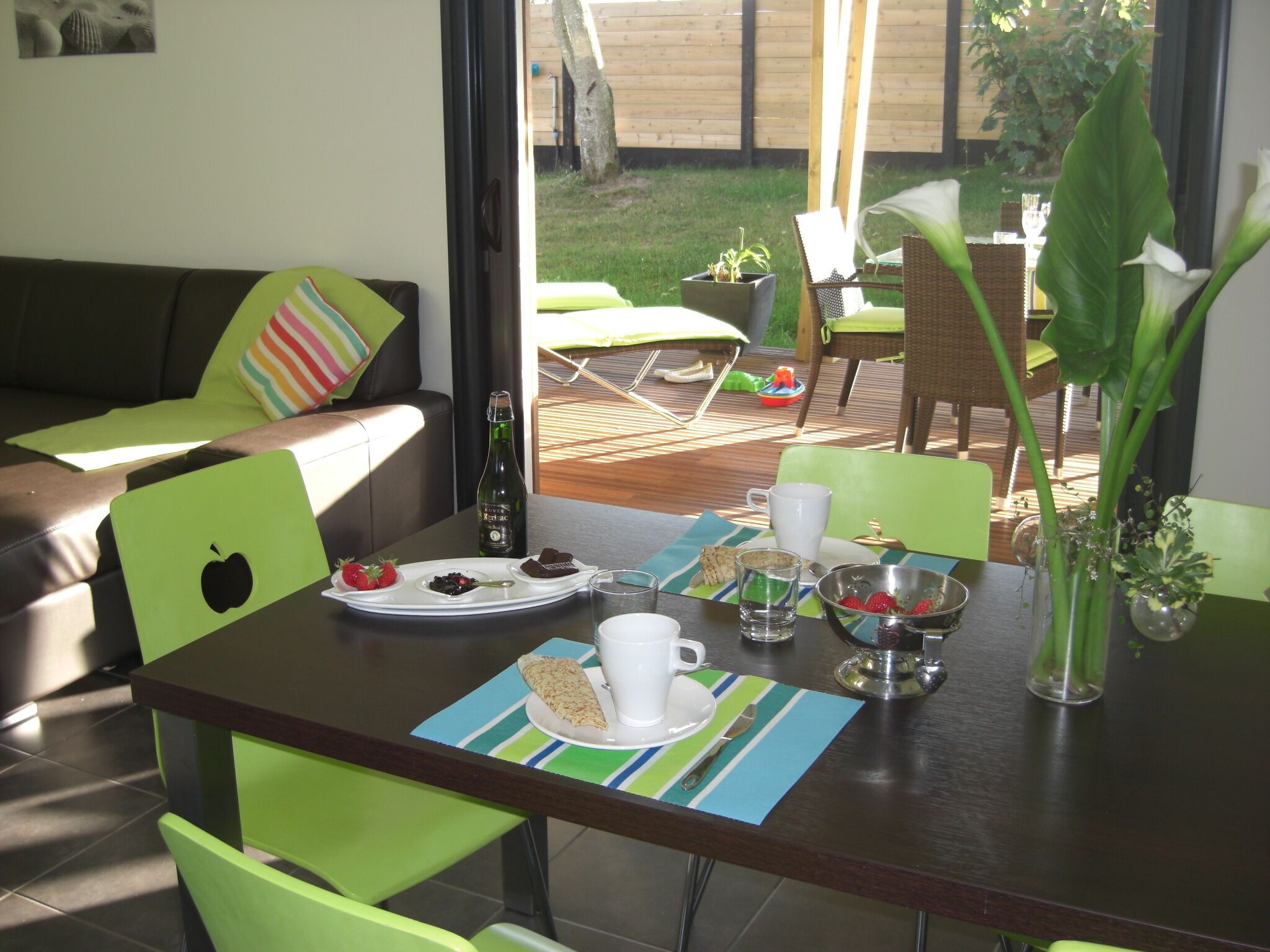 A dining area with a table set for breakfast, including a bottle, plates with food, and a vase with flowers.