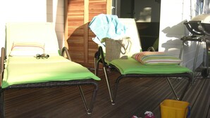 Deux fauteuils de jardin avec coussins, une chaise en osier et des jouets pour enfants sur une terrasse en bois.