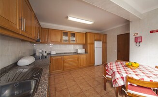 A kitchen with wooden cabinets, a stainless steel sink, a microwave, and a refrigerator. There is a dining table with a checkered tablecloth and chairs.