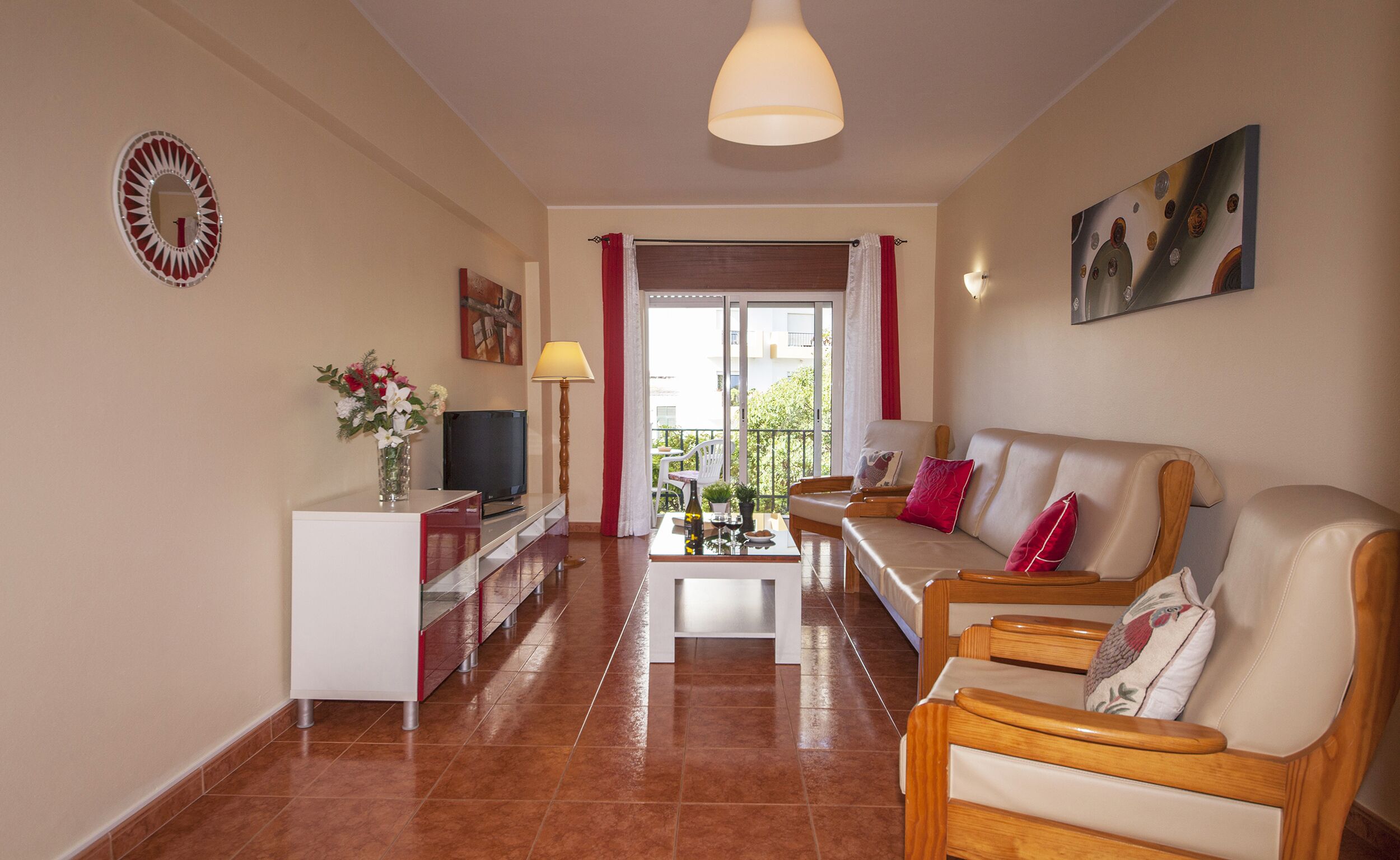 A living room with a sofa, armchairs, a coffee table, a TV, and a balcony with a view.